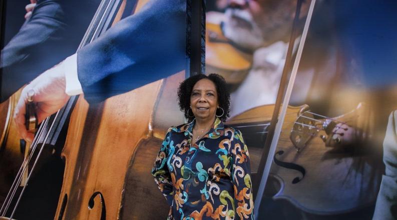 A woman in a patterned blouse stands in front of a mural 